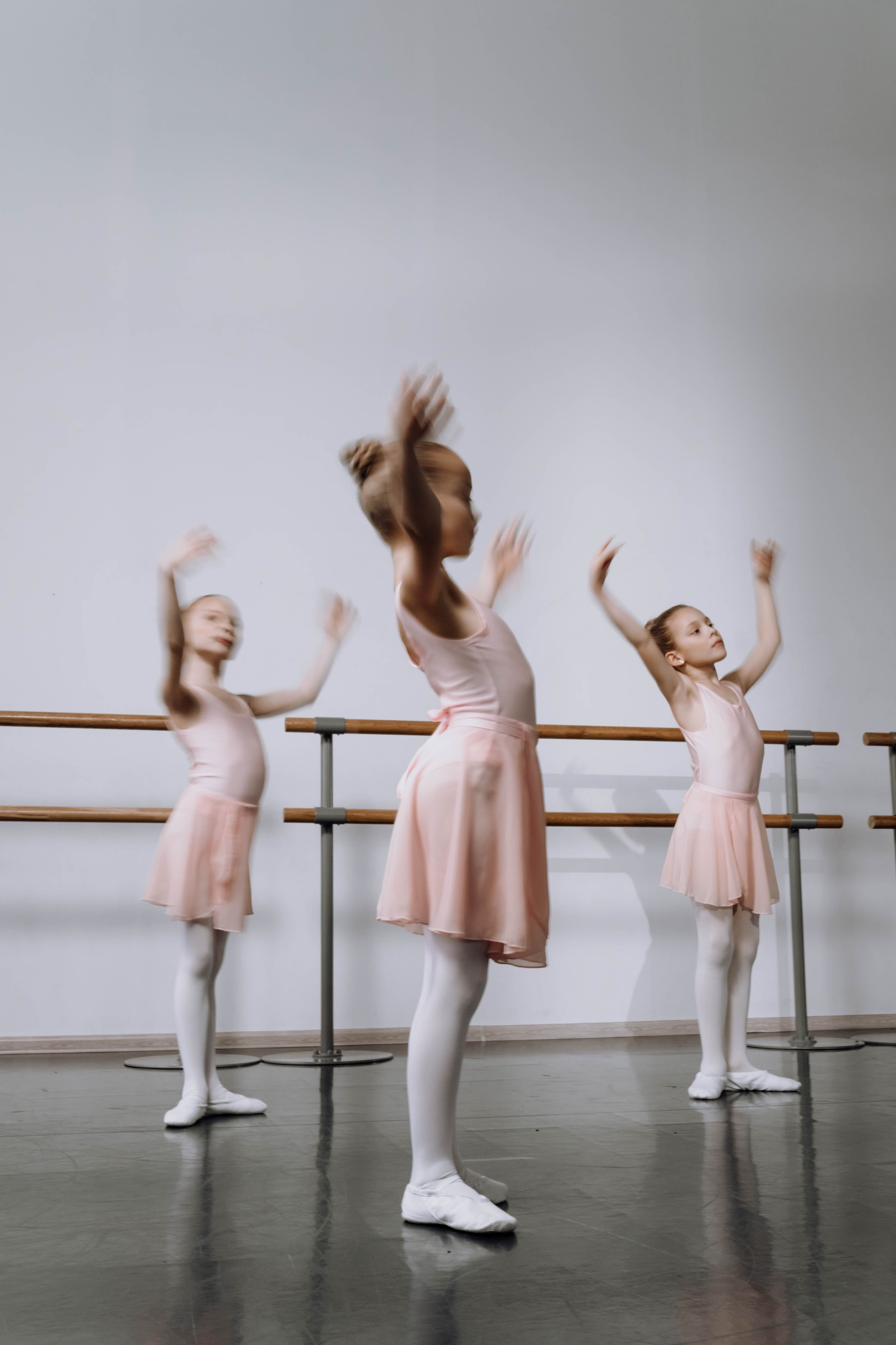 Three young ballet students practising expressive arm movements together at the studio barre